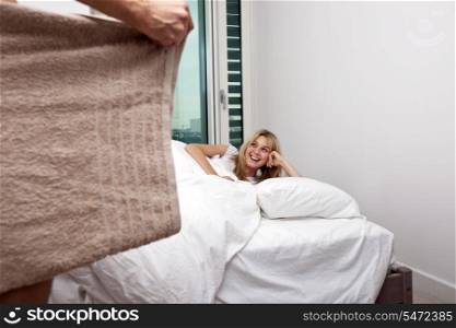 Happy woman looking at nude man holding towel in bedroom