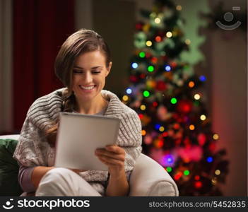 Happy woman looking in tablet PC in front of Christmas tree