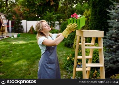 Happy woman looks on flower bed in the garden. Female gardener takes care of plants outdoor, gardening hobby, florist lifestyle and leisure. Happy woman looks on flower bed, gardening