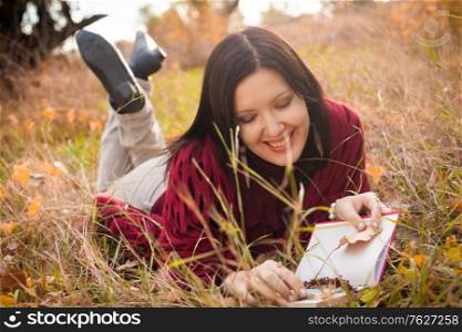 Happy woman lying down with book in the autumnal grass