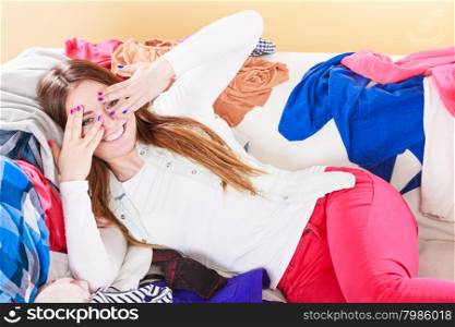 Happy woman lying on clothes covering eyes.. Portrait of happy glad young woman girl lying on stack of clothes covering eyes. Disorder and mess.