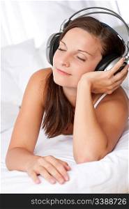 Happy woman lying on white sofa listening to music with headphones