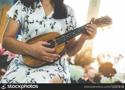 Happy woman musician playing ukulele and singing a song in sound studio. Music lifestyle concept.. Happy woman musician playing ukulele in studio.