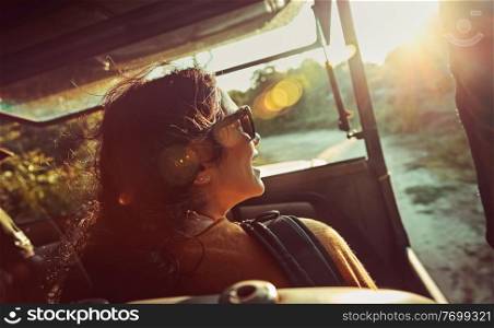 Happy woman on safari ride, pretty female enjoying trip along Sri Lanka, riding on a special convertible car and admires view on wild animals, active summer adventure
