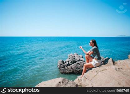 Happy woman outdoor on edge of cliff seashore enjoy the view on mountain top rock. Tourist woman outdoor on edge of cliff seashore