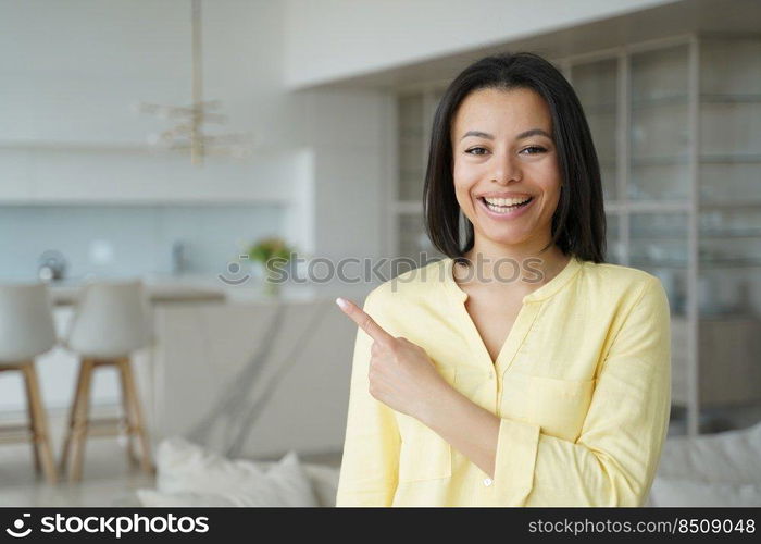 Happy woman points with finger to copy space. Conceptual portrait of young emotional woman. Advertising banner mockup. Handsome european girl in living room at home. Modern interior of apartment.. Happy woman handsome girl points with finger to copy space. Advertising banner mockup.