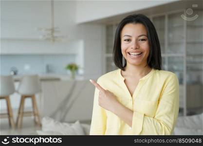 Happy woman points with finger to copy space. Conceptual portrait of young emotional woman. Advertising banner mockup. Handsome european girl in living room at home. Modern interior of apartment.. Happy woman handsome girl points with finger to copy space. Advertising banner mockup.