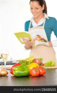 Happy woman preparing recipe vegetables wine kitchen cooking book