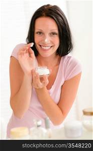 Happy woman putting cream on nose in bathroom