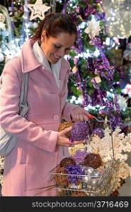 Happy woman putting sparkling Christmas decorations to shopping basket