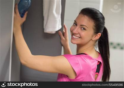 Happy woman putting water bottle in locker at gym
