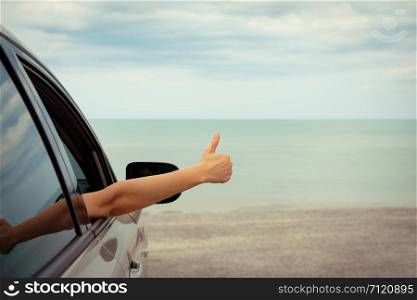 Happy woman raised arms from the car parked in the sea on a bright day. Vintage picture.