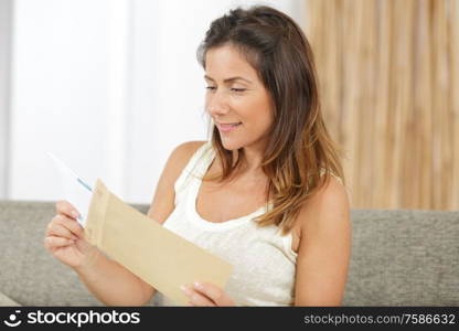 happy woman reading letter with good news sitting on sofa