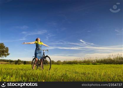 Happy woman relaxing and sitting on a bicycle, in a green meadow