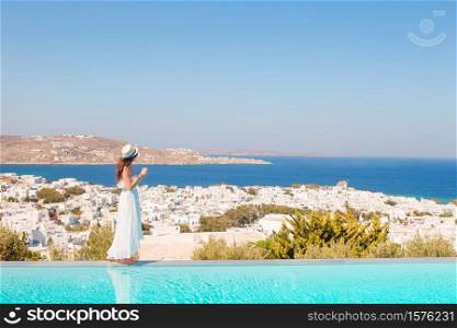 Happy woman relaxing on the edge of pool with amazing view on Mykonos, Greece. Beautiful woman enjoying summer vacation near pool