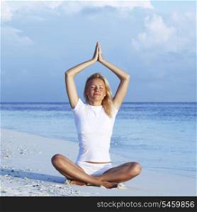 Happy woman sitting in yoga pose at the beach