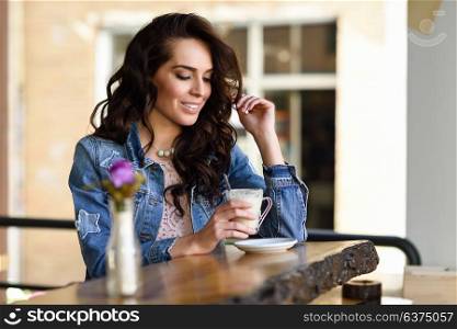 Happy woman sitting indoor drinking coffee. Cool young modern caucasian female in her 20s. Cafe city lifestyle.