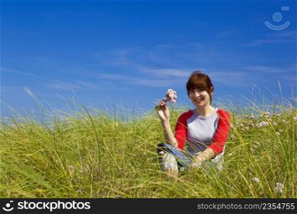 Happy woman sitting on a green meadow and holding flowers