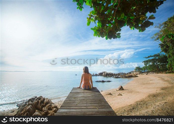 happy woman sitting on wood bridge with view of the sea, soft focus with noise