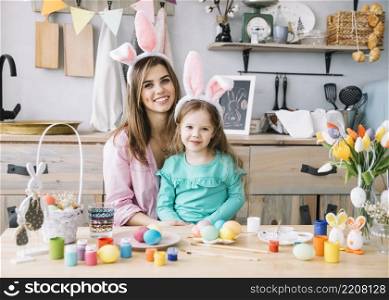 happy woman sitting with daughter bunny ears near easter eggs