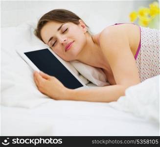 Happy woman sleeping embracing tablet PC