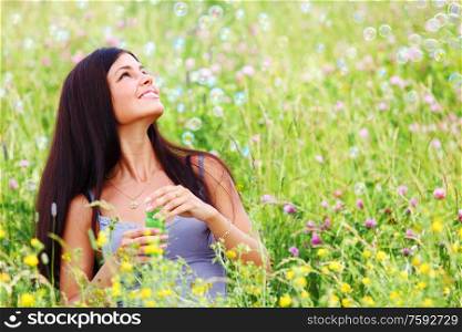 Happy woman smile in green grass soap bubbles around. Young girl blowing soap bubbles