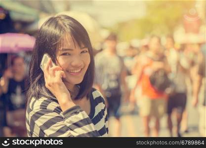 Happy woman smiling and walking in the street talking a smartphone and looking at camera. Vintage filtered image.
