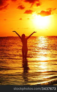 happy woman standing on a sunset in ocean waves