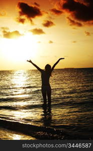 happy woman standing on a sunset in ocean waves