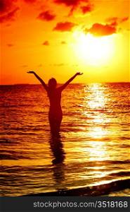 happy woman standing on a sunset in ocean waves