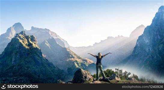 Happy woman stands with raised hands on background of sunset in mountain&rsquo;s range
