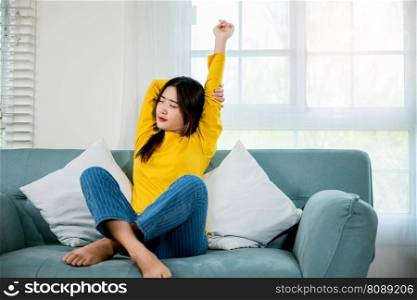 Happy woman stretch oneself for relaxing activity feeling lazy on weekend on couch, resting napping break, Lifestyle Asian young female stretching her arms on sofa in the living room at home