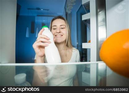 Happy woman taking bottle of milk out of refrigerator