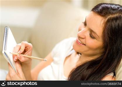 Happy woman taking notes into notepad using pencil