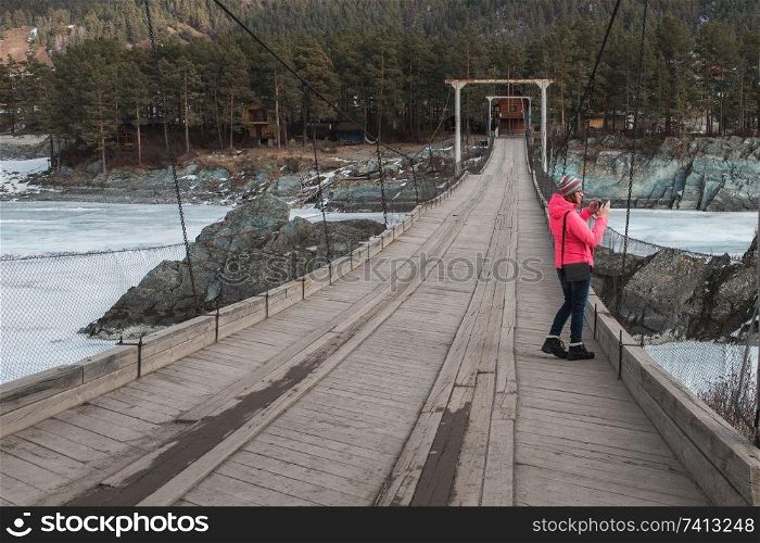Happy woman taking photos on the bridge from river at beauty sunny spring day, in Altai mountains. Travel vacation concept.. Happy woman taking photos on the bridge