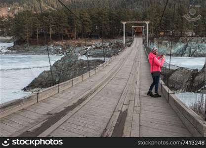 Happy woman taking photos on the bridge from river at beauty sunny spring day, in Altai mountains. Travel vacation concept.. Happy woman taking photos on the bridge