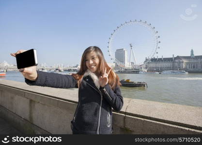Happy woman taking self portrait through cell phone against London Eye at London; England; UK