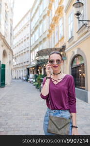 Happy woman talking by smartphone in european street. Young attractive tourist outdoors in Vienna city. Woman talk by her smartphone in city. Young attractive tourist outdoors in italian city