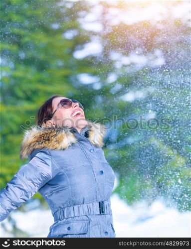 Happy woman throwing snow in wintertime park, enjoying nature, looking up, happy and active winter holidays, fun and joy concept