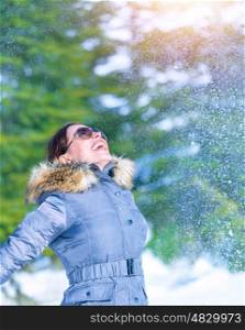 Happy woman throwing snow in wintertime park, enjoying nature, looking up, happy and active winter holidays, fun and joy concept