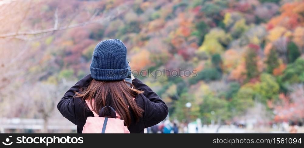 Happy woman tourist taking photo colorful leaves mountains by camera in Arashiyama, young Asian traveler visit in Kyoto, Japan. Fall Autumn season, Vacation, holiday and Sightseeing concept