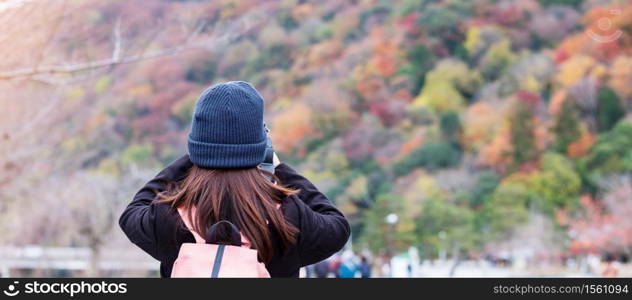 Happy woman tourist taking photo colorful leaves mountains by camera in Arashiyama, young Asian traveler visit in Kyoto, Japan. Fall Autumn season, Vacation, holiday and Sightseeing concept