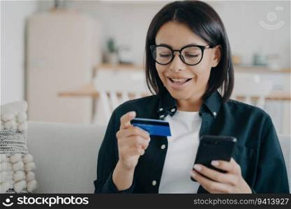 Happy woman uses online banking, makes secure money transfer with credit card and smartphone. Modern shopping at home. E-commerce, e-bank.