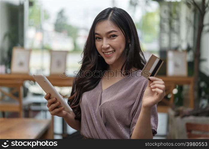 happy woman using credit card to shopping online with tablet at the cafe