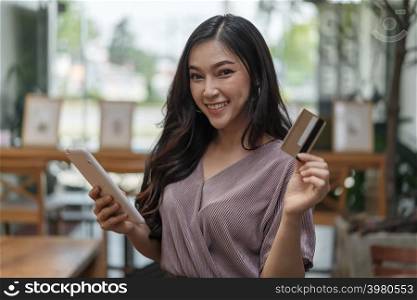 happy woman using credit card to shopping online with tablet at the cafe