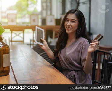 happy woman using credit card to shopping online with tablet at the cafe