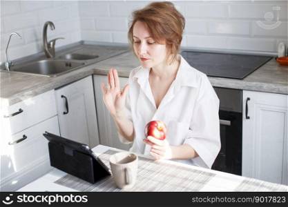 Happy woman using digital tablet for video call friends and parents. Happy beautiful woman with cup of coffee or tea using laptop in the kitchen in the white shirt.. Happy woman using digital tablet for video call friends and parents. woman with cup of coffee using laptop in kitchen