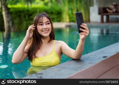 happy woman using smartphone to selfie a photo in the swimming pool