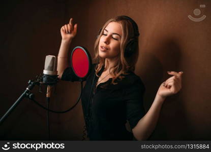 Happy woman vocalist in headphones against microphone, song record in music studio. Female singer recording audio track. Professional digital sound technologies