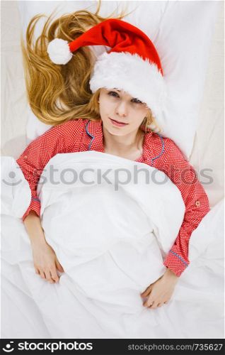 Happy woman waiting for Christmas season wearing pajamas and Santa Claus hat lying in bed.. Happy woman wearing pajamas and Santa Claus hat
